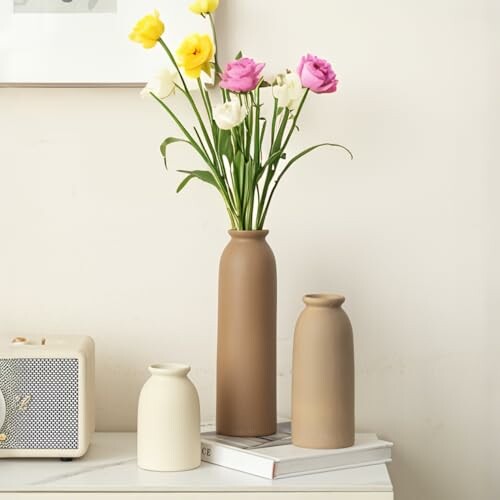 Colorful flowers in tall brown vase with two smaller vases on a table.