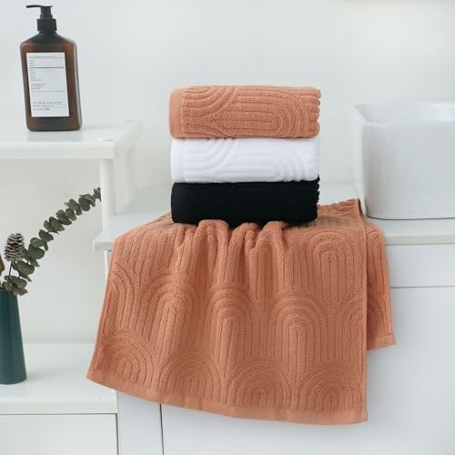 Stack of orange, white, and black towels on a bathroom counter with a soap dispenser and plant.