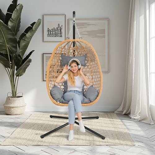 Woman sitting in a hanging chair indoors wearing headphones, enjoying a moment of relaxation.